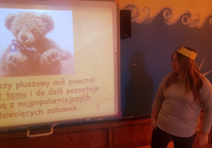 nauczycielka opowiada dzieciom o historii powstania Dnia Pluszowego Misia w oparciu o prezentację multimedialną